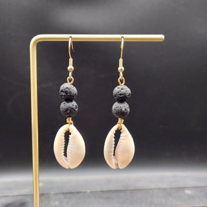 Peut inclure: Boucles d'oreilles dorées avec des perles de lave noire et des breloques en coquillage de cauris blanc.