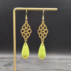 May include: A pair of gold earrings with a delicate, intricate design. Each earring features a teardrop-shaped green stone.