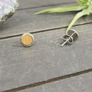 May include: A pair of silver stud earrings with a round wooden inlay. The wood is a light brown color and has a natural grain pattern.