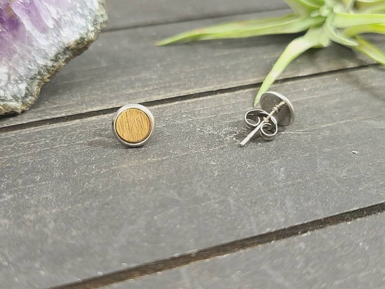 May include: A pair of silver stud earrings with a round wooden inlay. The wood is a light brown color and has a natural grain pattern.