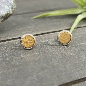 May include: A pair of gold and silver stud earrings with a circular design. The earrings have a wood-like texture.