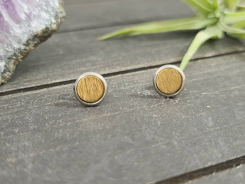 May include: A pair of gold and silver stud earrings with a circular design. The earrings have a wood-like texture.
