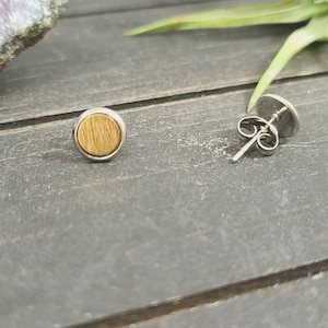 May include: A pair of small, round earrings with a wood grain design. The earrings are made of stainless steel and have a silver finish.