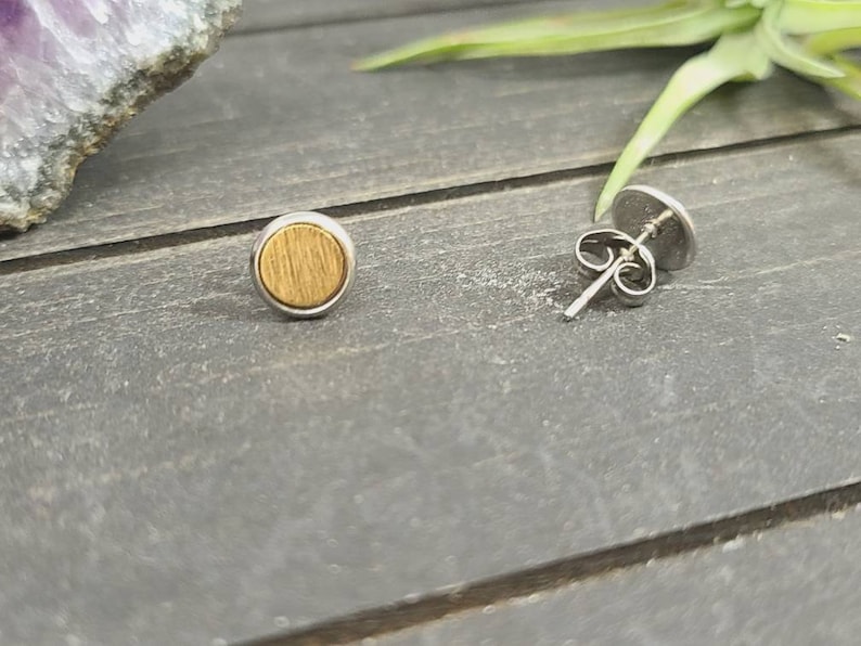 May include: A pair of small, round earrings with a wood grain design. The earrings are made of stainless steel and have a silver finish.