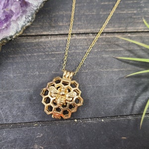 May include: A gold necklace featuring a bee charm within a honeycomb pendant.