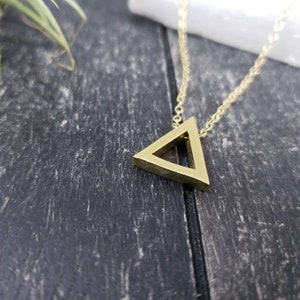 May include: A gold-toned necklace with a hollow triangle pendant. The pendant is made of metal and has a simple, geometric design.