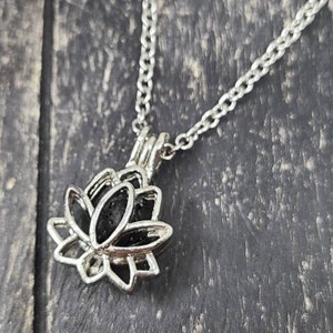 May include: A silver chain necklace with a silver lotus flower pendant. The pendant is open and has a black interior.