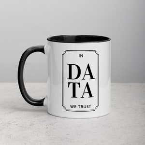 May include: White ceramic mug with a black rim and handle. The mug has a black graphic that says "In Data We Trust" in a decorative font.