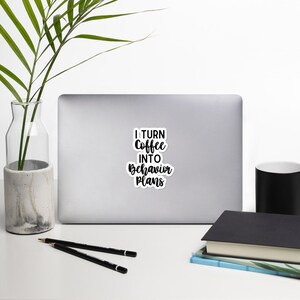 May include: A white laptop with a black and white sticker that says "I turn coffee into behaviour plans".
