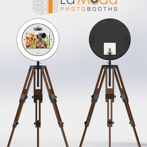 May include: A white ring light photo booth with a black and white screen displaying a woman in a swimsuit. The photo booth is mounted on a brown wooden tripod.