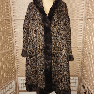 May include: A long brown and gold tweed coat with a faux fur collar and trim. The coat has a hood and a long, flowing silhouette.