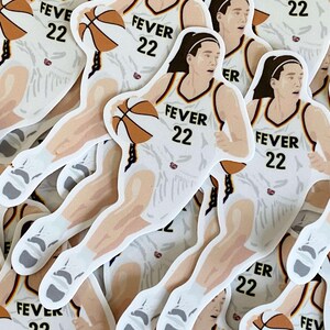 May include: A stack of white basketball player stickers with the text "FEVER 22" on the front. The player is wearing a white jersey with purple and orange accents. The player is holding a basketball.