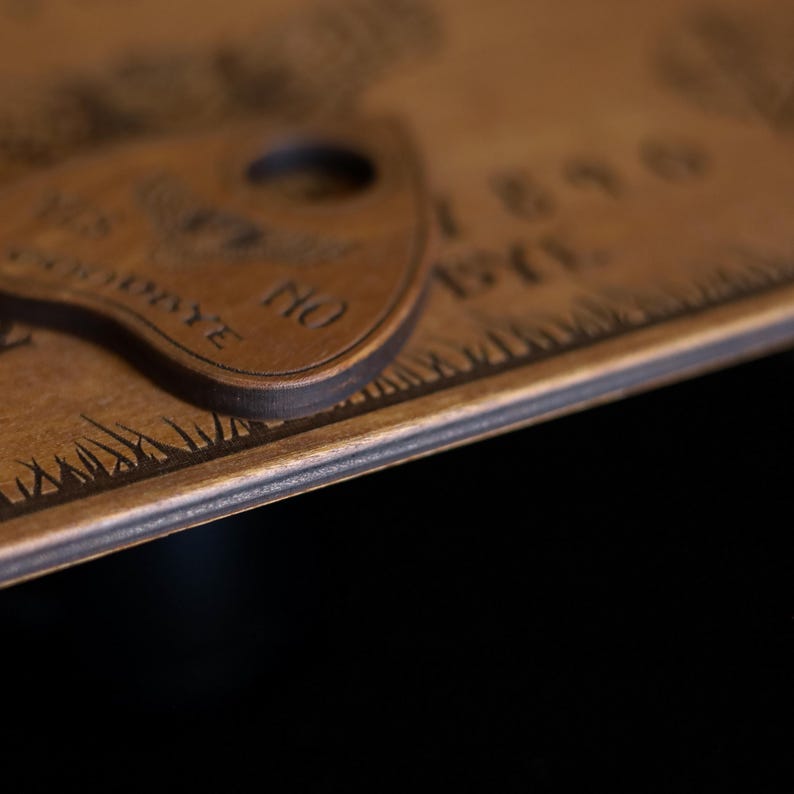 Op de afbeelding: Close-up van een houten Ouija-bord met een planchette. Het bord is gegraveerd met letters, cijfers en de woorden "JA", "NEE" en "TOT ZIENS". De planchette heeft een afgeronde vorm met een gat in het midden.