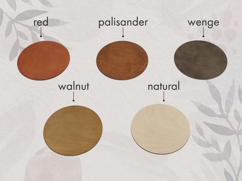 Op de afbeelding: Een verzameling van vijf houten onderzetters in verschillende kleuren: rood, palissander, wenge, walnoot en naturel. Elke onderzetter is rond met een glad oppervlak. De namen van de kleuren staan boven elke onderzetter.