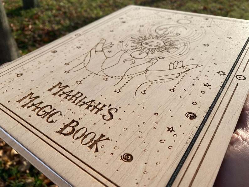 May include: A wooden journal with a sun and moon design and the text "Mariah's Magic Book" engraved on the front.