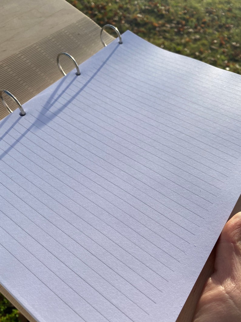 May include: A white notebook with lined pages and a silver binder. The notebook is open and lying flat on a wooden surface.