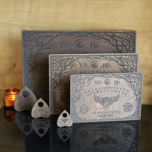 Op de afbeelding: Een verzameling houten Ouija-borden en planchette-aanwijzers. De borden zijn gegraveerd met letters, cijfers en de woorden "Ja" en "Nee". De planchette-aanwijzers hebben een rond kijkgaatje. De borden hebben een uil- en takontwerp.