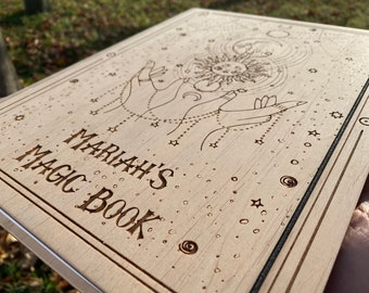 May include: A wooden journal with a sun and moon design and the text "Mariah's Magic Book" engraved on the front.