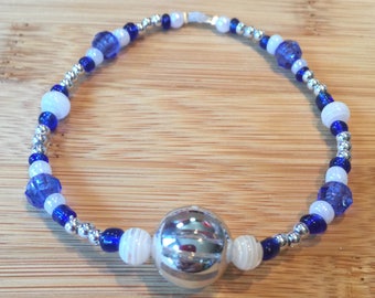 May include: A silver charm bracelet with blue and white beads. The bracelet has a large silver charm in the center.