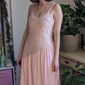 May include: A long pink dress with a lace bodice and a flowing skirt. The dress has a scoop neckline and thin straps.