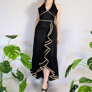 May include: A black halter dress with gold trim and a ruffled skirt. The dress is made of a silky fabric and has a fitted bodice.