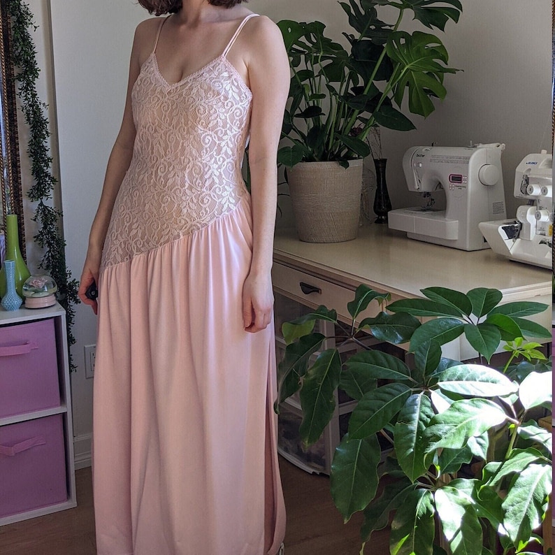 May include: A long pink dress with a lace bodice and a flowing skirt. The dress has a scoop neckline and thin straps.