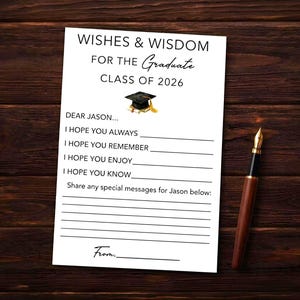 May include: A white graduation card with the text "Wishes & Wisdom For The Graduate Class of 2026" and fill-in-the-blank prompts. A gold-tipped pen rests beside the card on a dark wood surface.