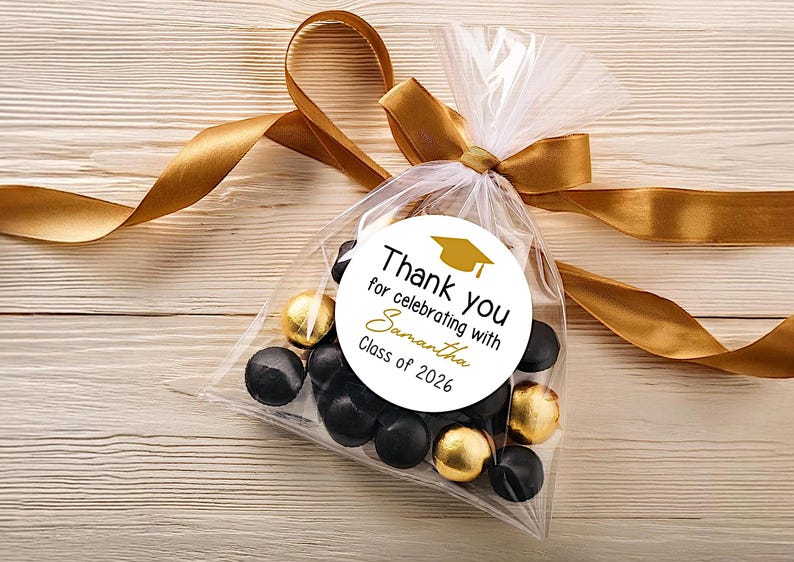 May include: A clear plastic favor bag filled with black and gold foil-wrapped candies, tied with a gold satin ribbon. A circular white sticker features a gold graduation cap icon and the text: Thank you for celebrating with Samantha Class of 2026.