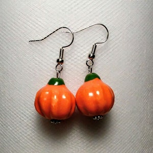 May include: A pair of orange and green pumpkin dangle earrings with silver hooks.