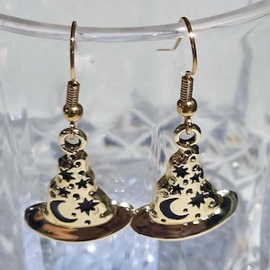May include: A pair of gold-toned dangle earrings shaped like pointed hats. Each hat features a black enamel crescent moon and star pattern on the front, suspended from gold-colored metal fishhook ear wires for pierced ears.