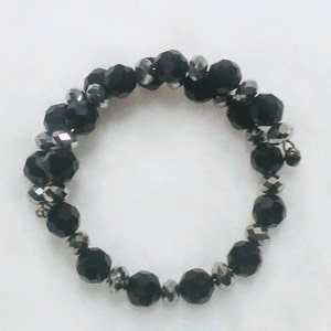 May include: A black beaded bracelet with silver accents. The beads are faceted and have a shiny finish.