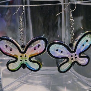 May include: A pair of butterfly-shaped earrings. Each earring features a black outline with a rainbow-colored interior and small, dotted accents. The earrings hang from silver-colored hooks and chains.