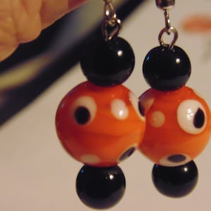 May include: Orange and black polka dot earrings with silver hooks. The earrings are made of glass beads and have a whimsical design.