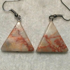 May include: A pair of triangle-shaped earrings with a white base and red and gold marbling. The earrings have silver hooks.