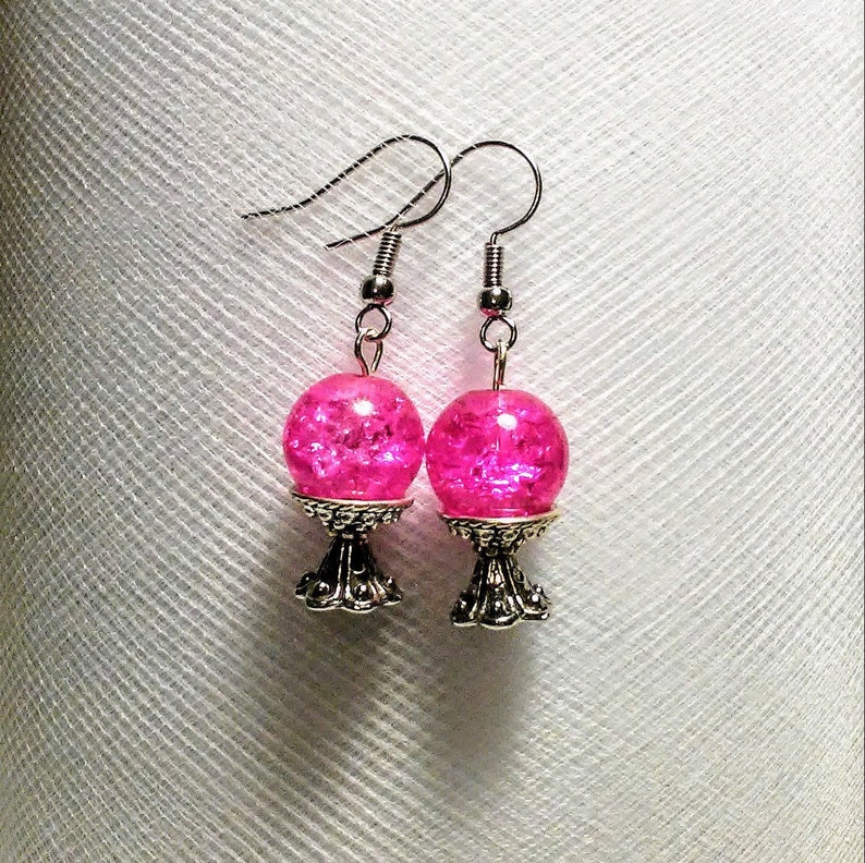 May include: A pair of silver earrings with pink glass spheres on top of a silver stand.