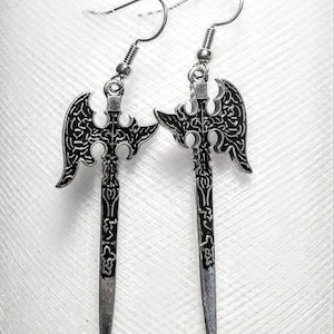 May include: A pair of silver earrings shaped like swords with intricate black detailing. The swords have a blade and a decorative axe head.