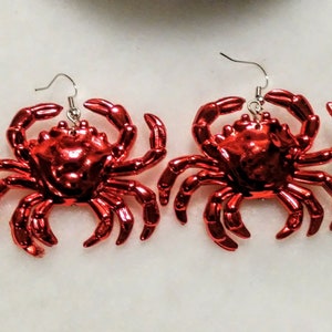 May include: A pair of red crab earrings. The crabs are made of shiny, metallic red plastic and have silver hooks.