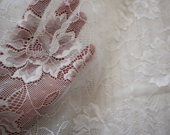 May include: White lace fabric with a delicate floral pattern. The lace is soft and sheer, with a subtle sheen.