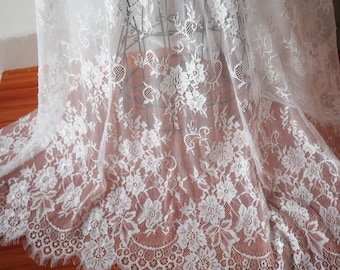 May include: White lace fabric with a delicate floral pattern and scalloped edge. The lace is sheer and has a soft, flowing texture.