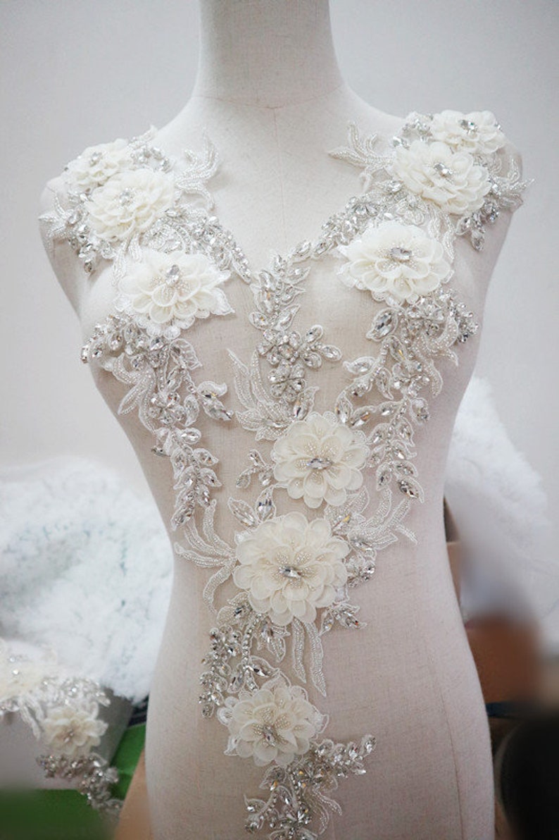 May include: White beaded and floral applique with rhinestones. This embellishment is perfect for adding a touch of elegance to wedding dresses, bridal gowns, or other formal wear.