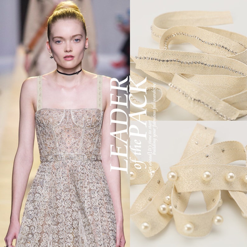 May include: Two beige fabric trims with different embellishments. One trim has a row of small white pearls and the other has a row of silver rhinestones.