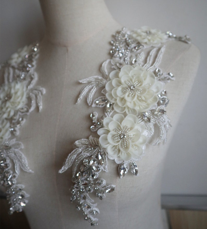 May include: Two white floral appliques with pearl and rhinestone embellishments. The appliques are perfect for adding a touch of elegance to wedding dresses, bridal accessories, or other special occasion garments.