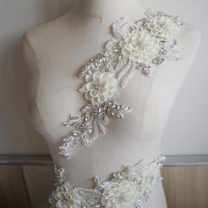 May include: White floral applique with silver beading and rhinestones. The applique is perfect for adding a touch of elegance to wedding dresses, bridal accessories, or other special occasion garments.