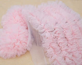 Può includere: Primo piano di un tessuto di tulle rosa chiaro con bordi arricciati. Il tessuto è disposto in un motivo a strati, creando un aspetto morbido e strutturato. Il tulle è probabilmente utilizzato per scopi decorativi, come nell'abbigliamento o nell'artigianato.