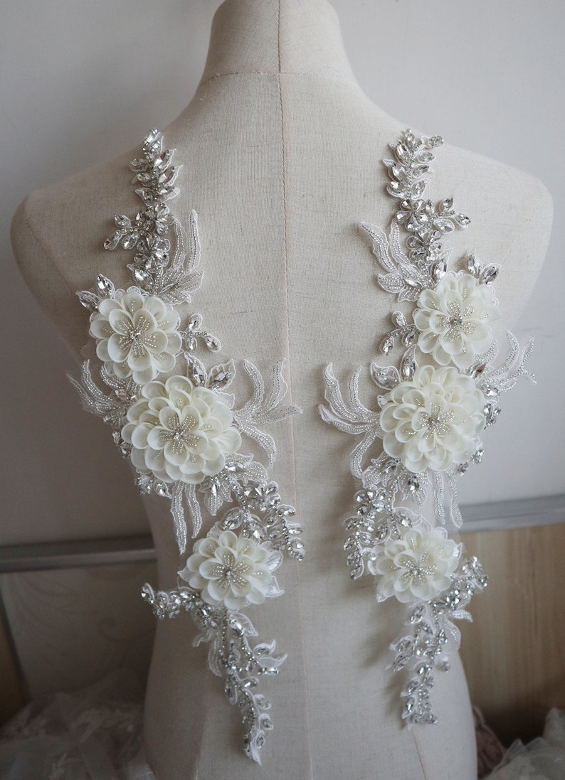 May include: Two white floral appliques with silver rhinestone embellishments. The appliques are on a white mannequin.