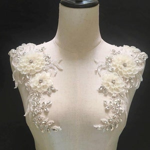 May include: Two white floral appliques with silver beading and sequins. The appliques are perfect for adding a touch of elegance to wedding dresses, bridal accessories, or other special occasion garments.