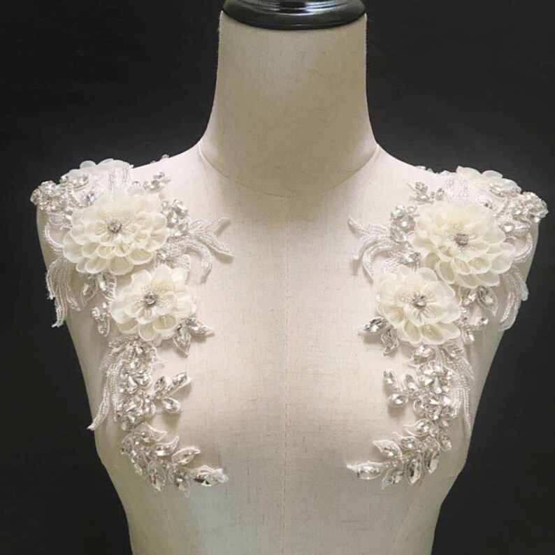 May include: Two white floral appliques with silver beading and sequins. The appliques are perfect for adding a touch of elegance to wedding dresses, bridal accessories, or other special occasion garments.