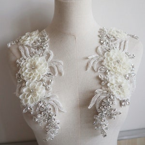 May include: Two white floral appliques with silver beading and rhinestones. The appliques are perfect for adding a touch of elegance to a wedding dress or other special occasion garment.