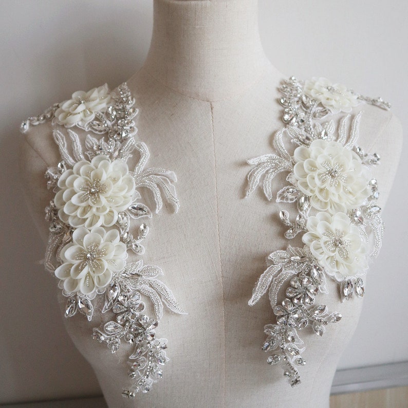 May include: Two white floral appliques with silver beading and rhinestones. The appliques are perfect for adding a touch of elegance to a wedding dress or other special occasion garment.