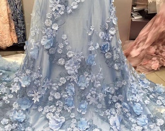 Può includere: Tessuto di tulle azzurro con applicazioni floreali 3D. Il tessuto è decorato con fiori delicati di diverse dimensioni e forme.